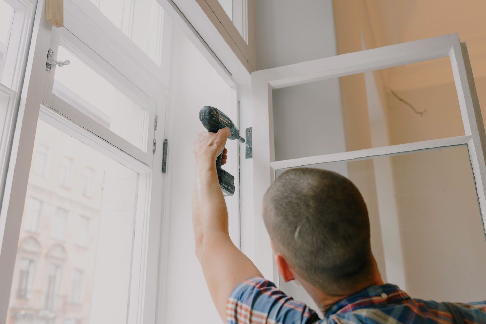 Back view of unrecognizable craftsman using cordless screwdriver and assembling window while screwing in Riverside, CA
